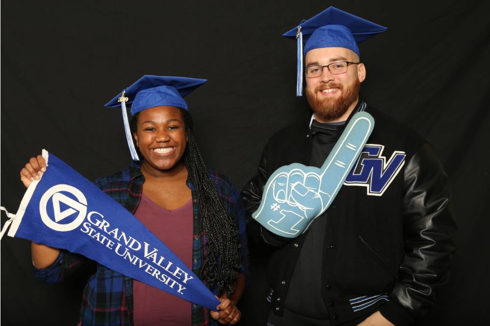 two friends with grad caps and gvsu flag